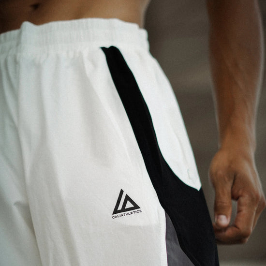 White athletic shorts with a black side stripe and a black triangular logo on the left leg, worn by a male model.