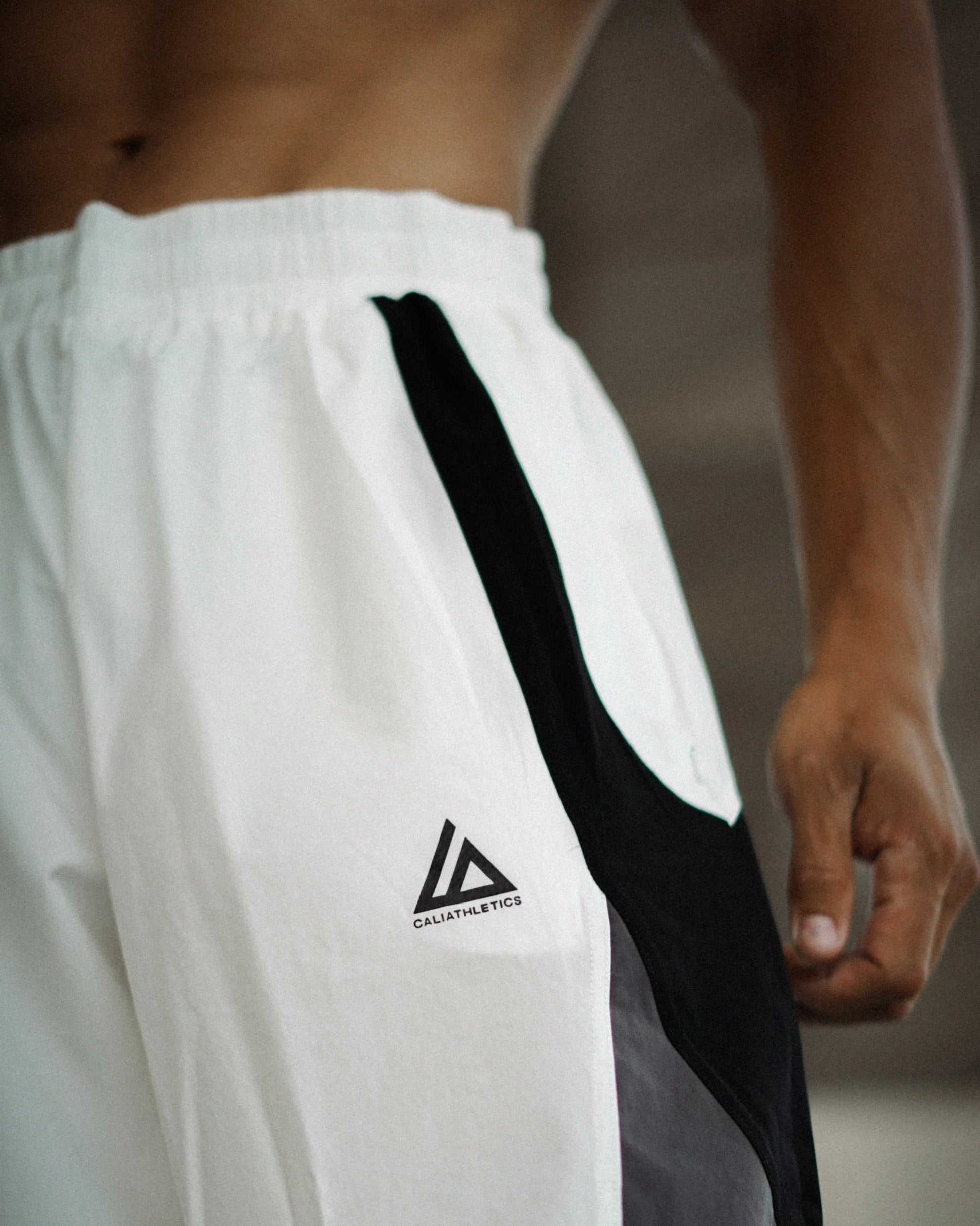 White athletic shorts with a black side stripe and a black triangular logo on the left leg, worn by a male model.
